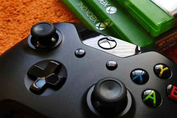Un contrôleur Xbox posé sur le sol à côté d'une pile de jeux Xbox One.