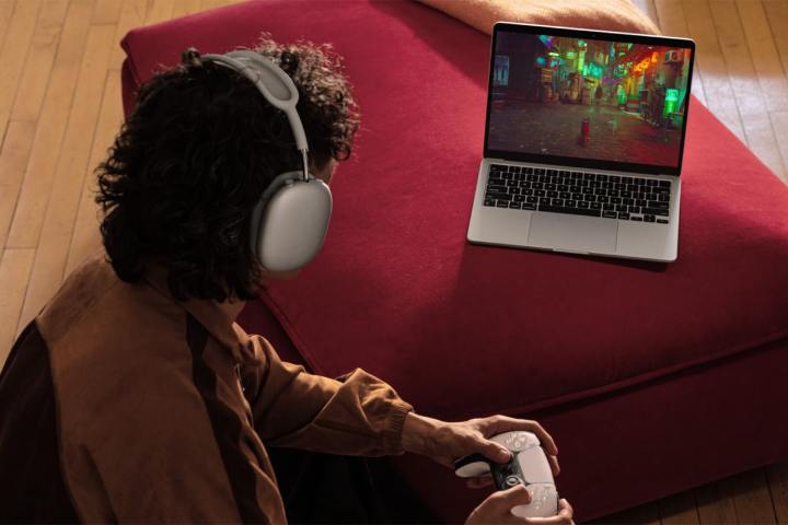 Une personne joue à Stray avec une manette PlayStation sur un MacBook Air argenté de 13 pouces.