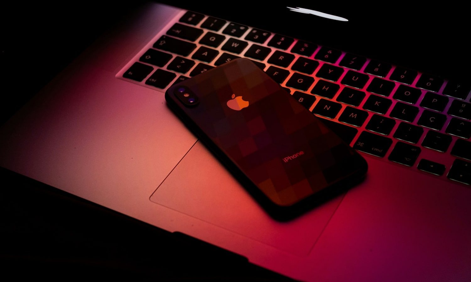 Un MacBook et un iPhone sous une lumière rouge foncé.