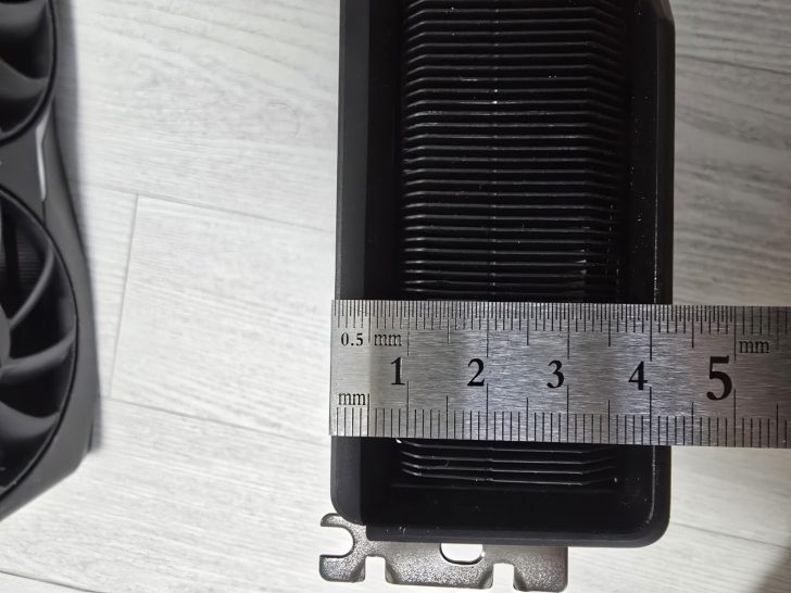 Mètre ruban mesurant le refroidisseur de carte graphique sur un sol en bois blanc.