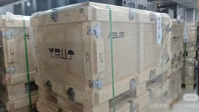 Wooden shipping crates with ASUS logo stacked in a warehouse, wrapped and secured for transport.