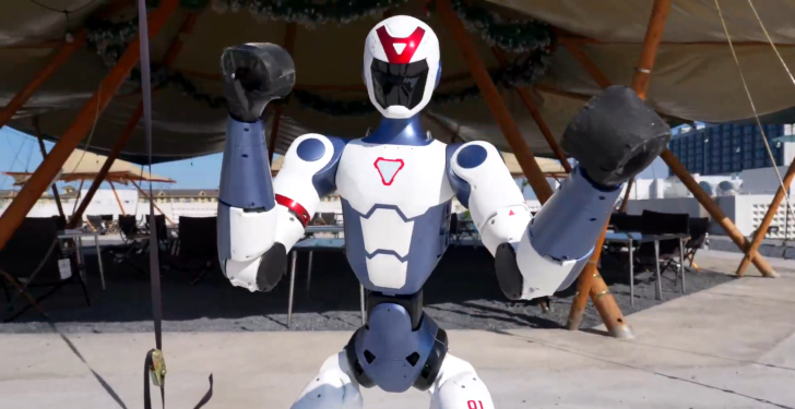 Robot humanoïde levant les poings, montrant une technologie avancée en extérieur.