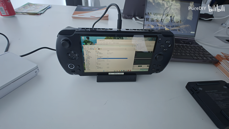 Console de jeu portable sur un bureau connectée à un moniteur avec un ordinateur portable en arrière-plan.
