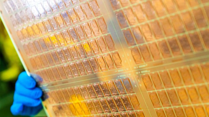 Main gantée tenant un wafer de semiconductor avec des circuits complexes.
