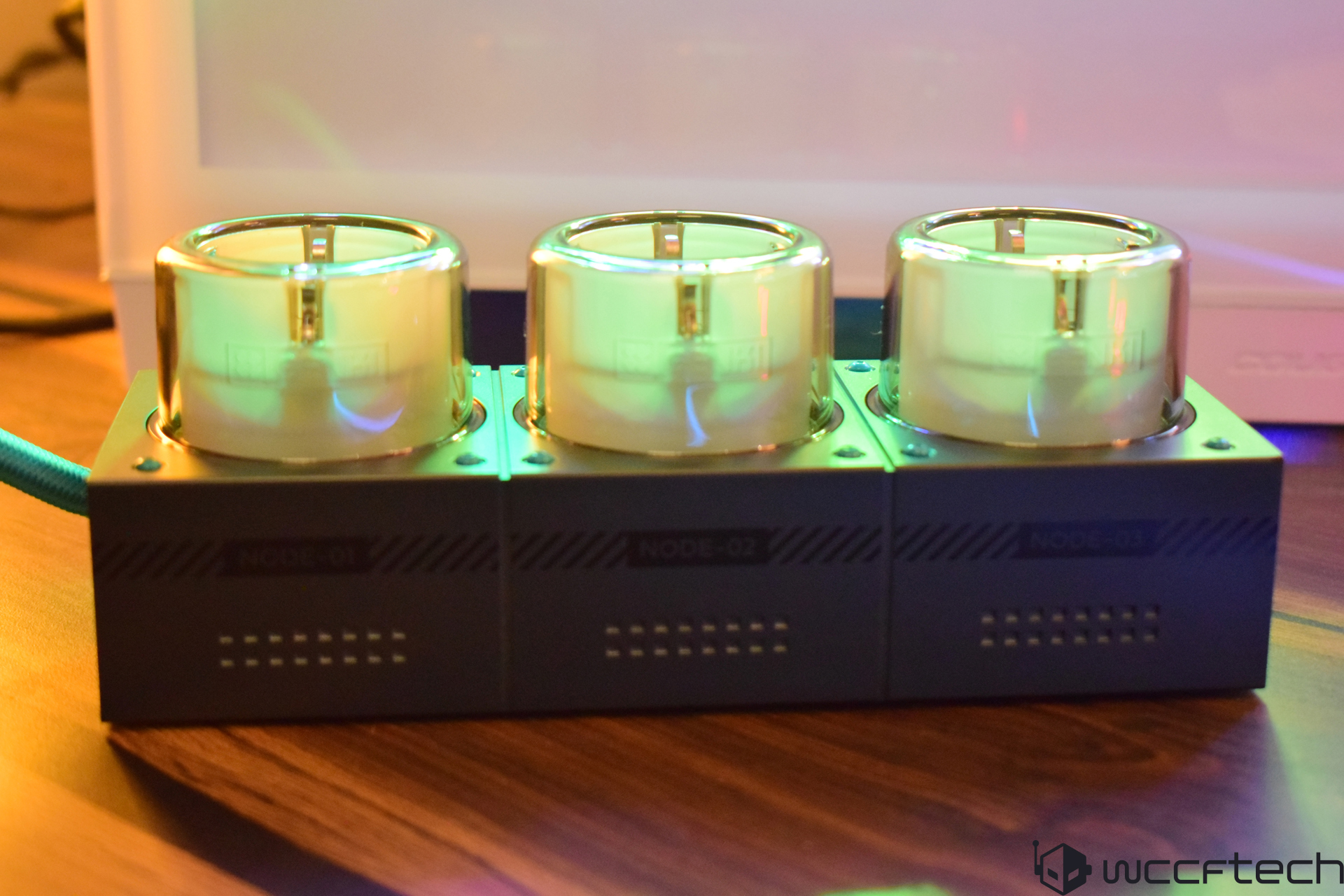 Three glowing computer cooling components on wooden surface.
