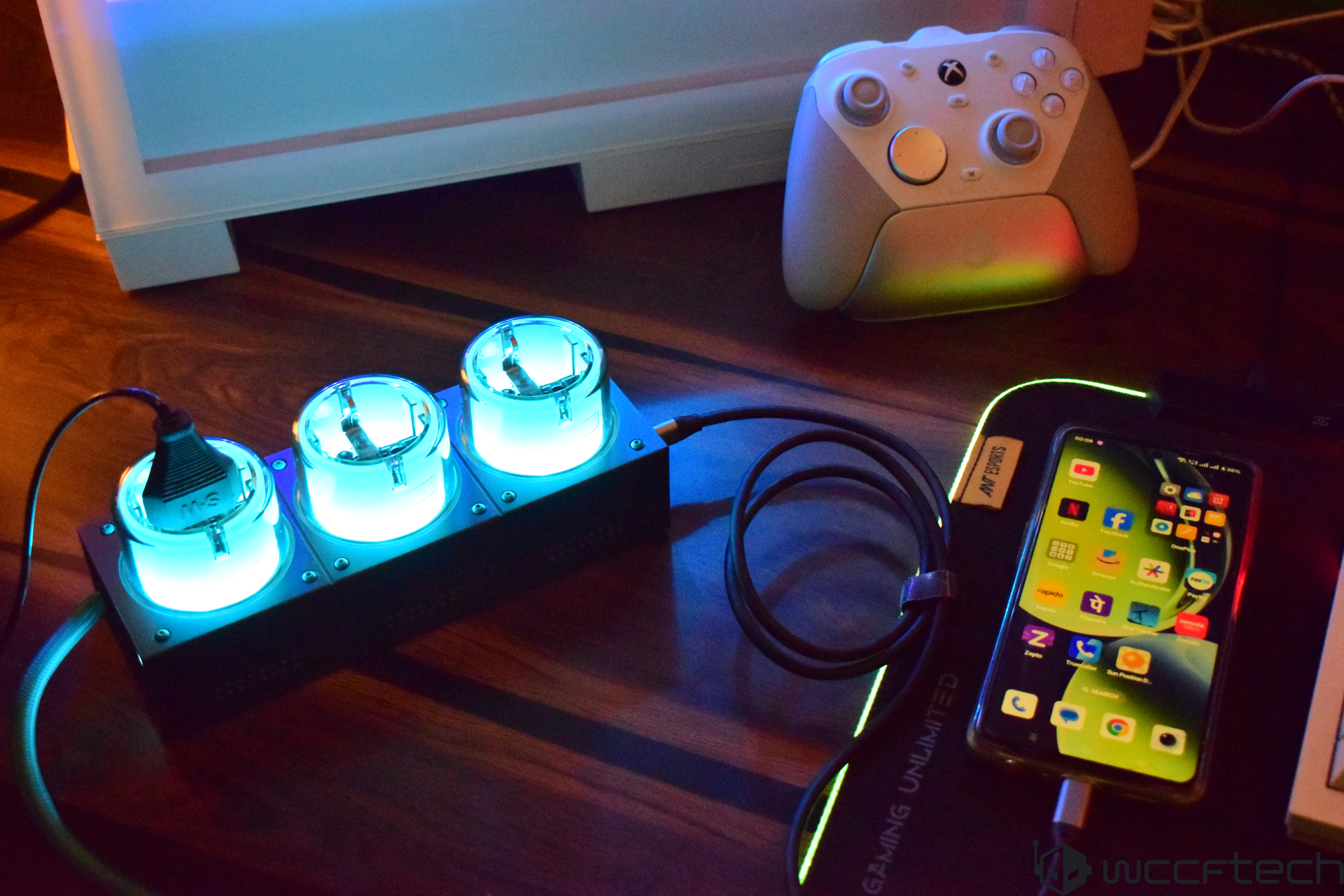 Gaming setup with glowing tech gadgets, charger, and a controller on a desk.
