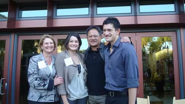 Quatre personnes souriant devant un bâtiment avec de grandes fenêtres.
