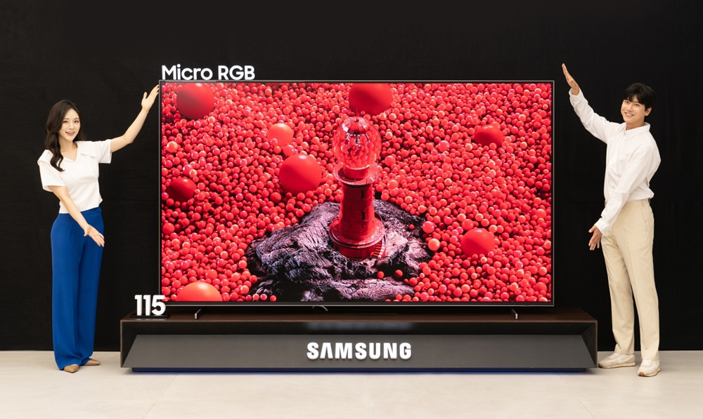 Deux personnes présentent le TV Samsung 115 pouces Micro RGB avec des visuels rouges vibrants.