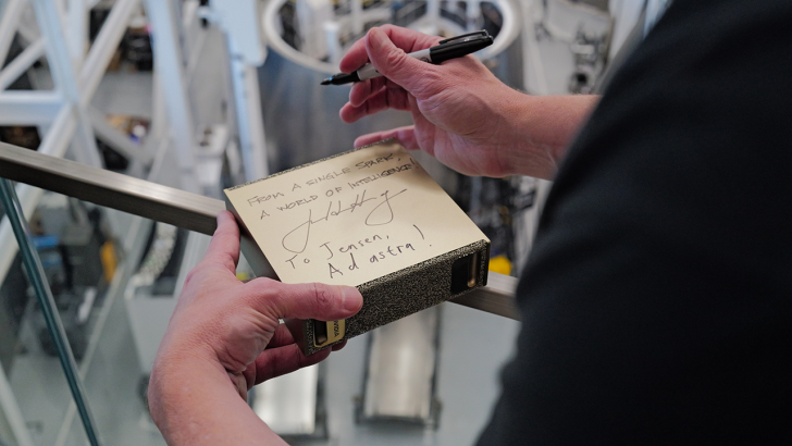 NVIDIA box with handwritten message From a single spark: a world of intelligence! held by a person with a black marker.