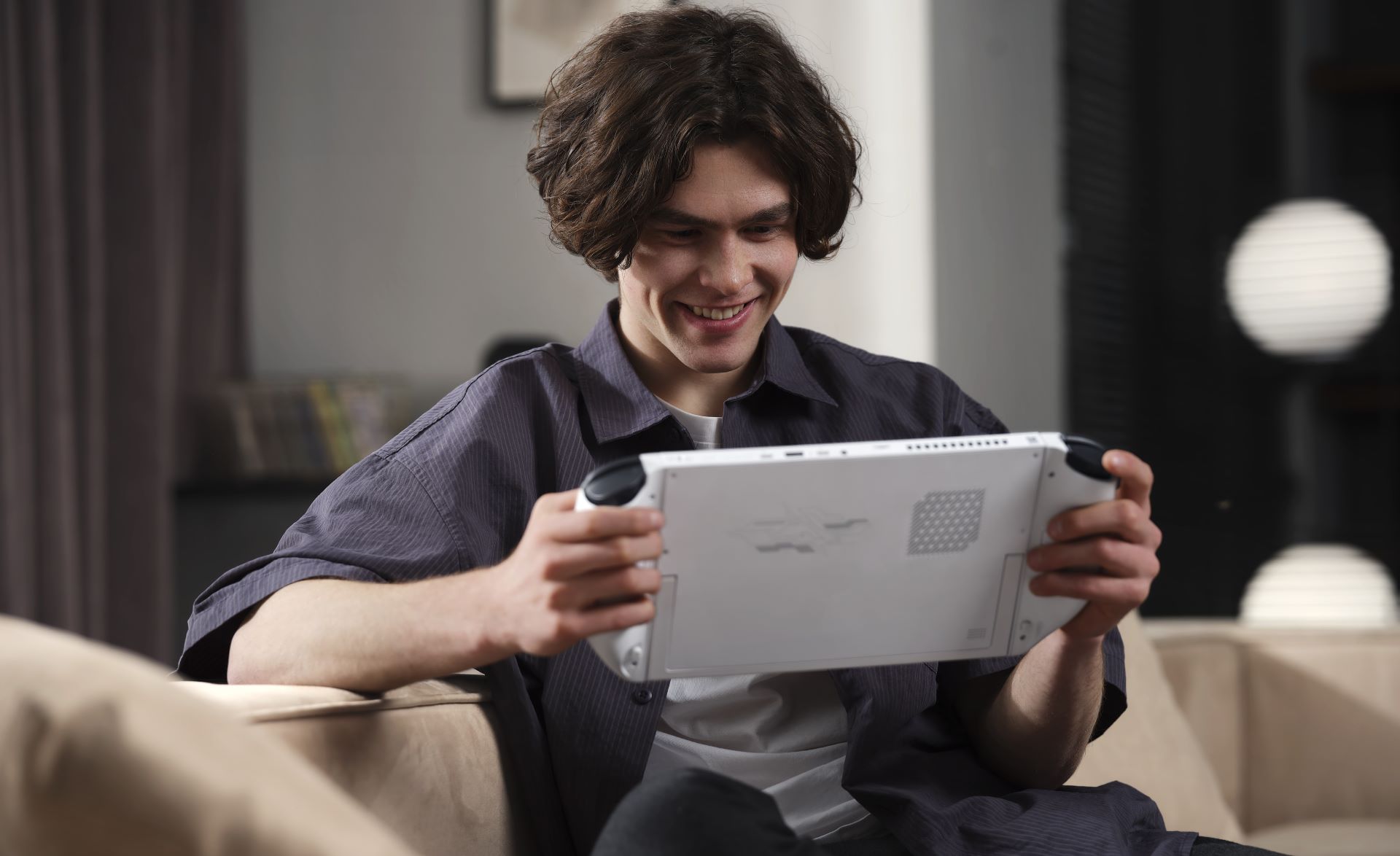 Personne souriante tenant un appareil de jeux portable sur un canapé.