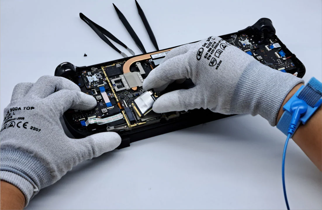 Deux mains gantées travaillant sur une Steam Deck, montrant ses composants internes.