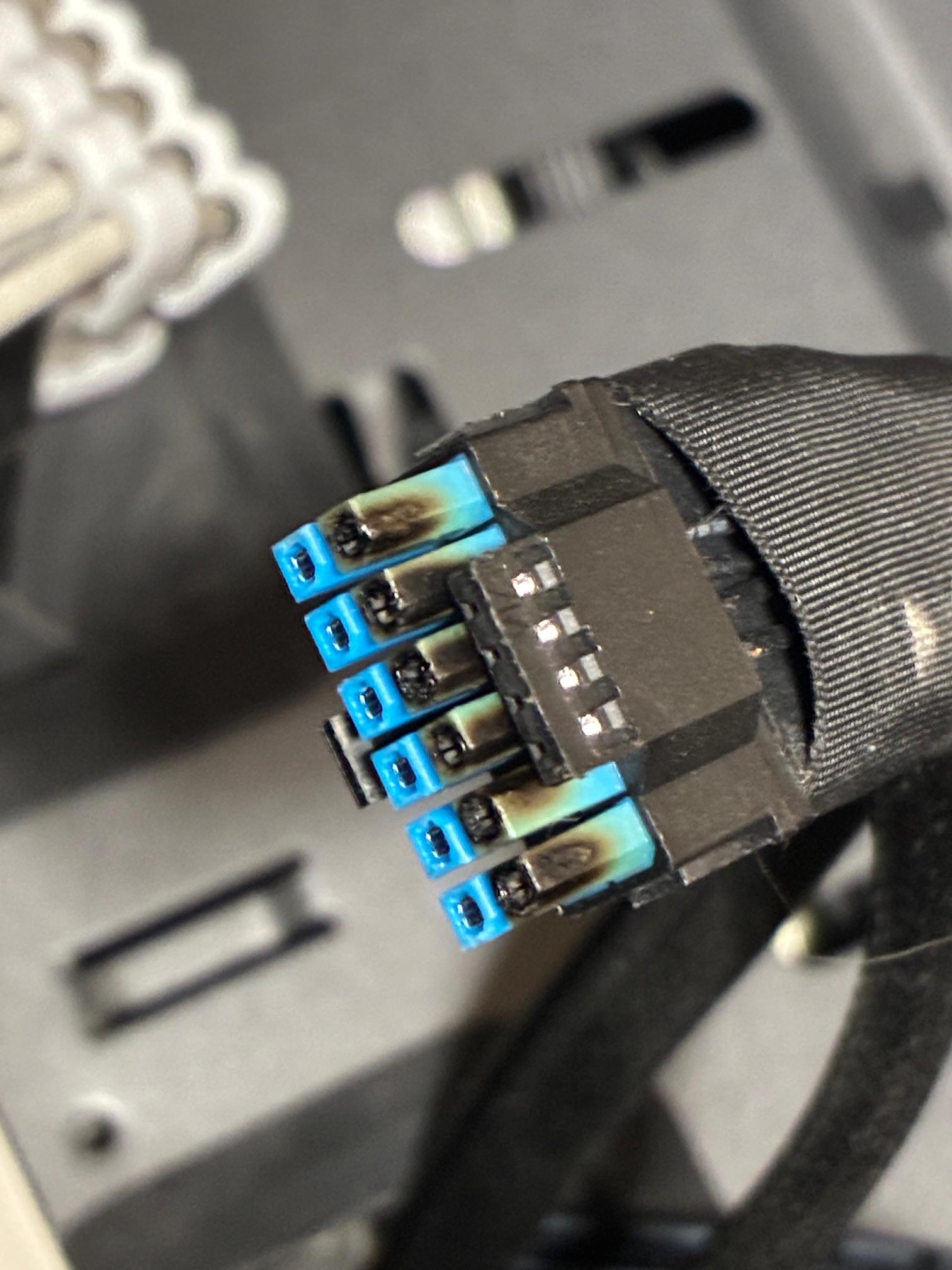 Connecteur d'alimentation 16 broches partiellement fondu avec des broches bleues et noires, montrant des signes de surchauffe.