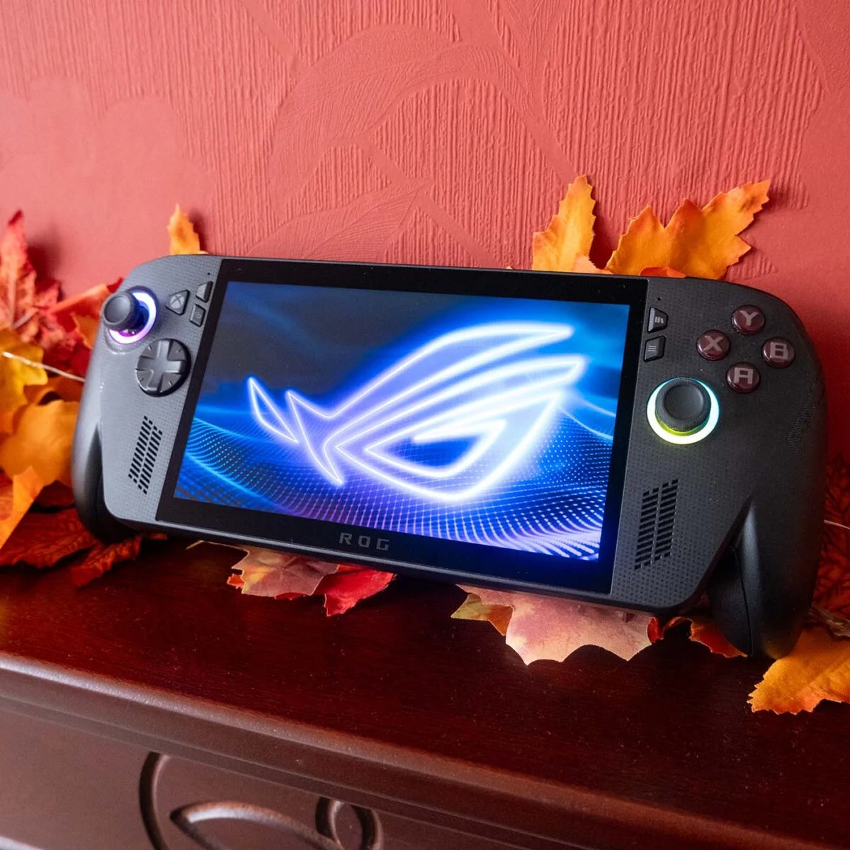ROG Xbox Ally X against a red backdrop with autumnal foliage.