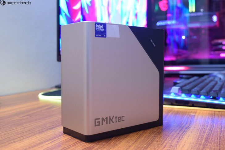 Mini PC GMKtec avec Intel Core Ultra 9 sur un bureau en bois à côté d'un moniteur coloré.