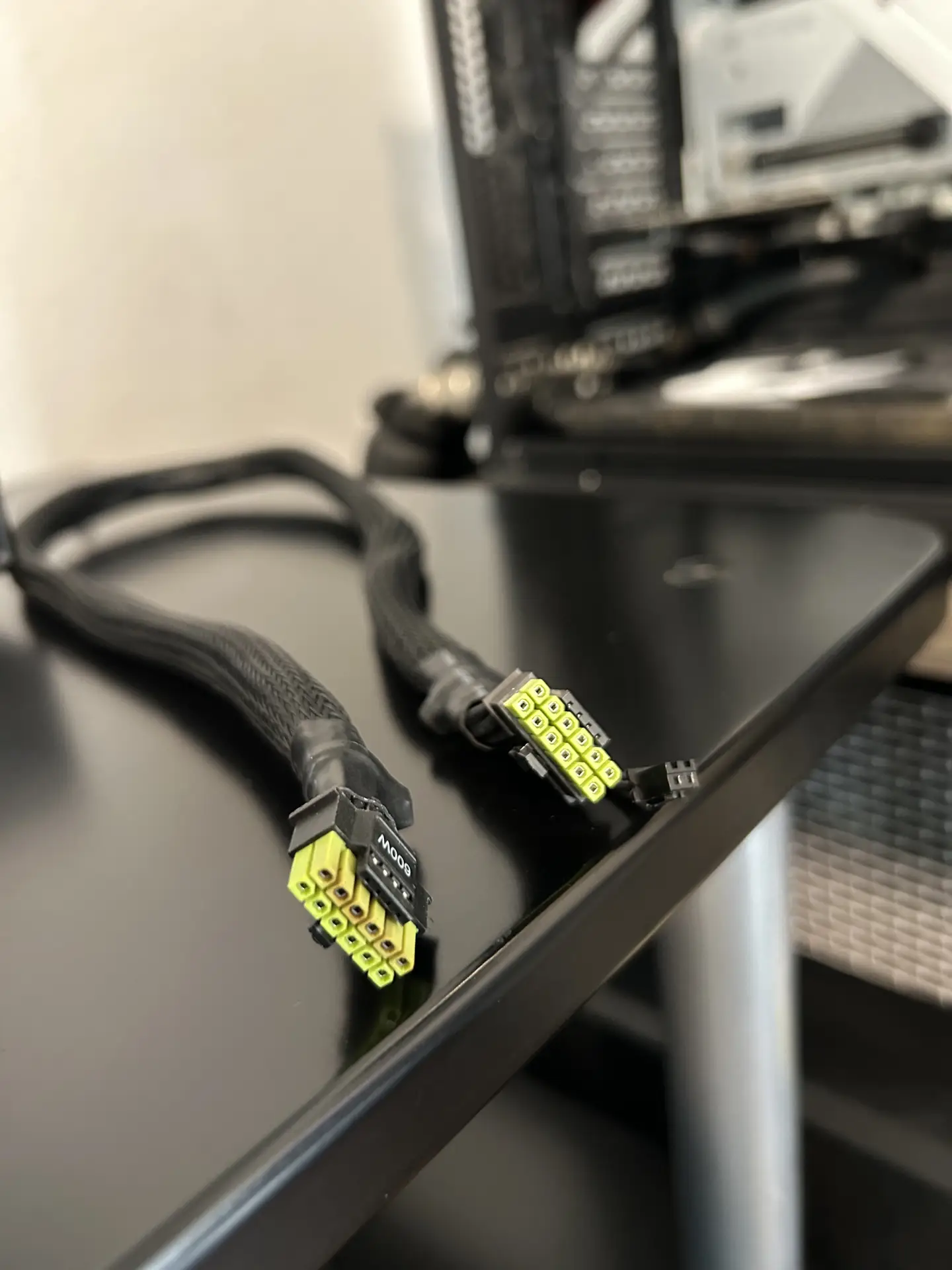 Deux connecteurs d'alimentation tressés noirs de 600W avec des broches jaunes sur fond noir, avec une unité centrale en arrière-plan.