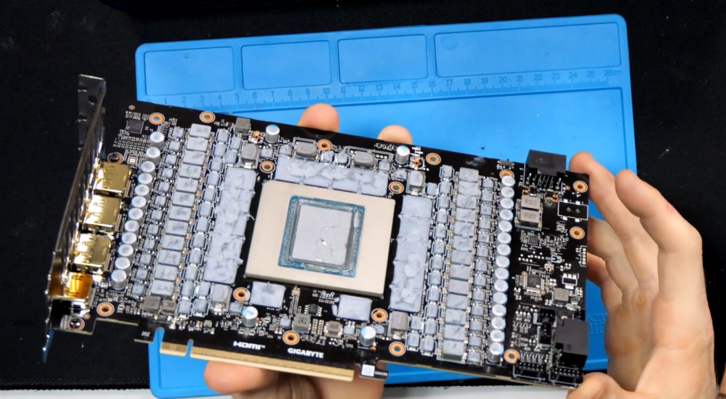 Une personne tenant une carte graphique Gigabyte avec de la pâte thermique visible et plusieurs condensateurs, placée sur une surface anti-statique