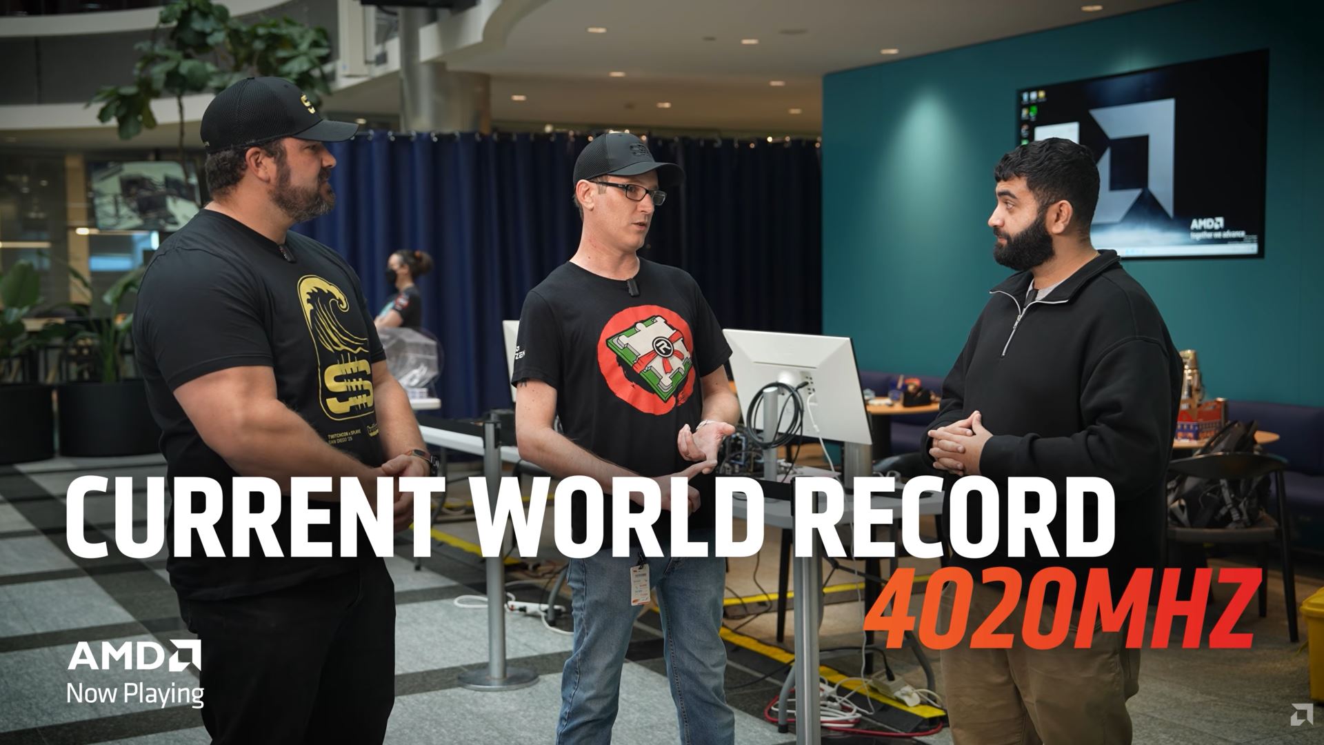 Trois hommes discutent près d'un ordinateur, avec un fond à thème AMD