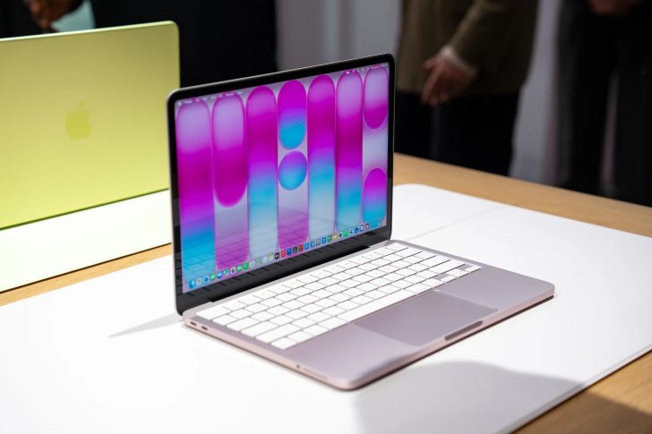 Un MacBook d'Apple ouvert sur une table, affichant un fond abstrait coloré, avec un autre MacBook fermé en jaune