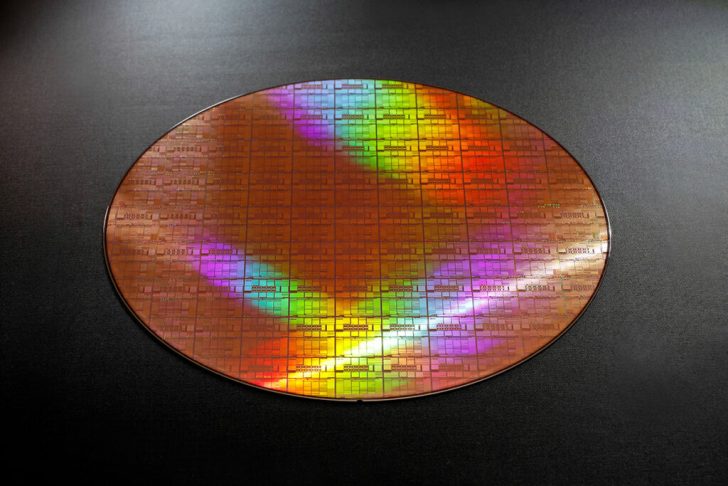 Un wafer de semi-conducteurs coloré réfléchissant des teintes arc-en-ciel sur une surface sombre.