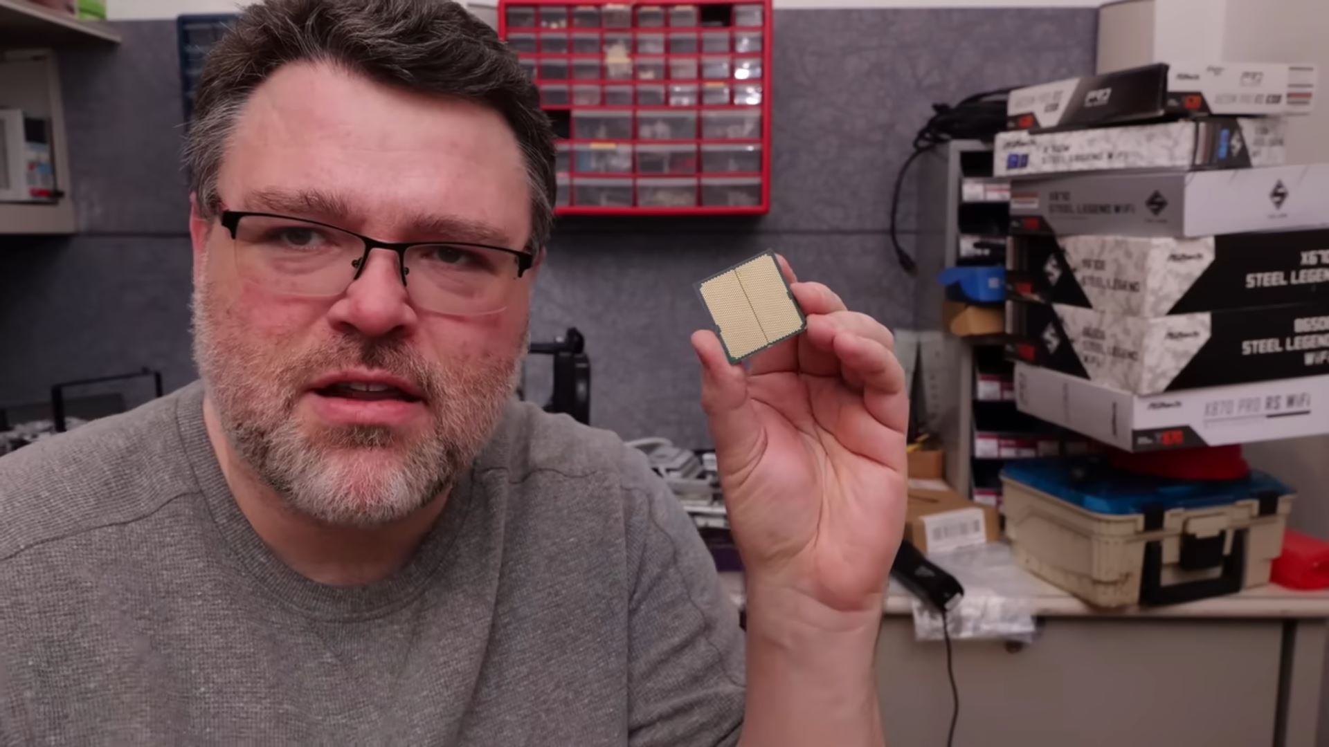 Un utilisateur tenant un processeur dans une pièce avec des boîtes de cartes mères ASRock en arrière-plan.