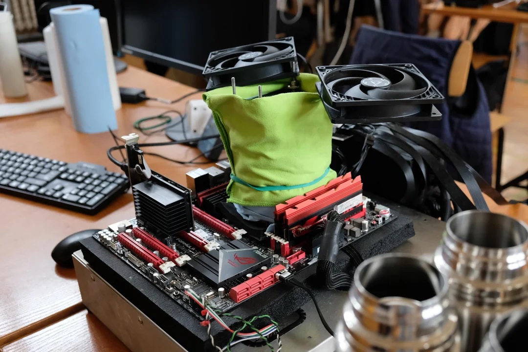 An ASUS Republic of Gamers motherboard is set up on a test bench with liquid nitrogen cooling and dual fans for overclocking purposes.