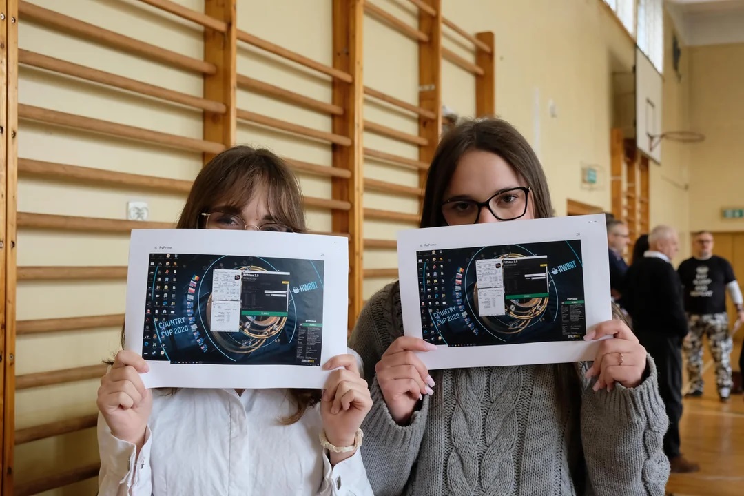 Two individuals hold up printed screenshots displaying the HWBot 'Country Cup 2020' benchmark results with visible desktop icons.