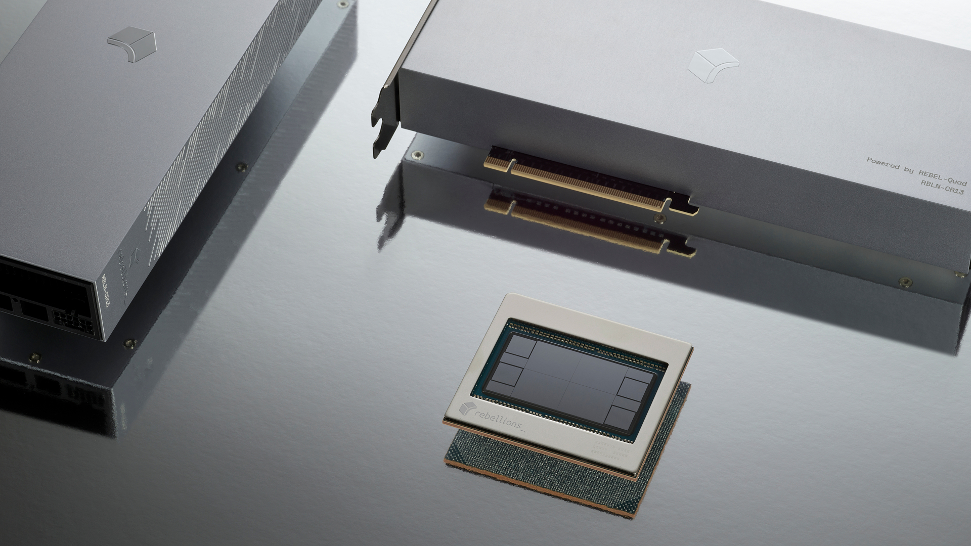 A Rebellions electronics chip and a PCI card labeled 'Powered by REBEL-Qude RBLN-CR43' are displayed on a reflective surface.