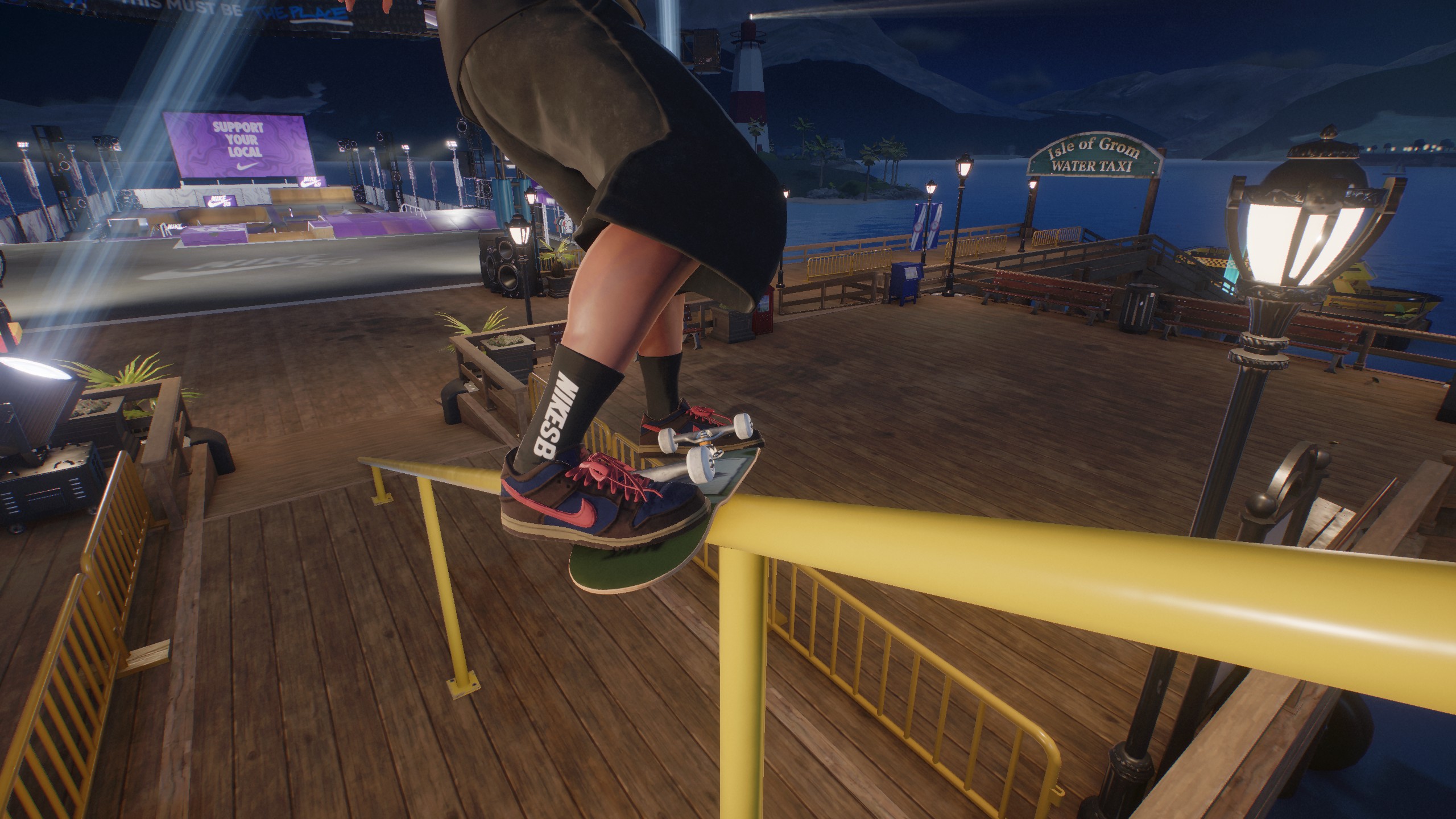 A skateboarder wearing Nike SB socks performs a grind on a yellow rail at a nighttime skate park with a sign for 'Isle of Grom Water Taxi' in the background.