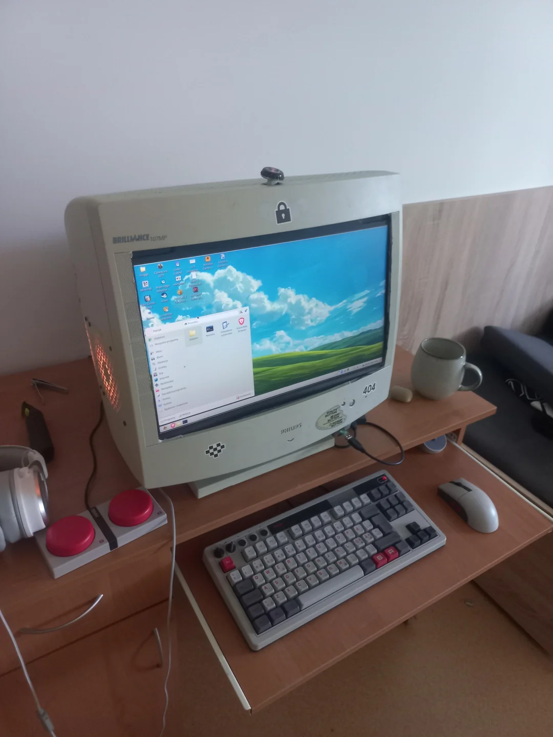 A Philips Brilliance 107MP CRT monitor displaying the Windows XP desktop theme on a wooden desk with a vintage keyboard, mouse, and headphones.