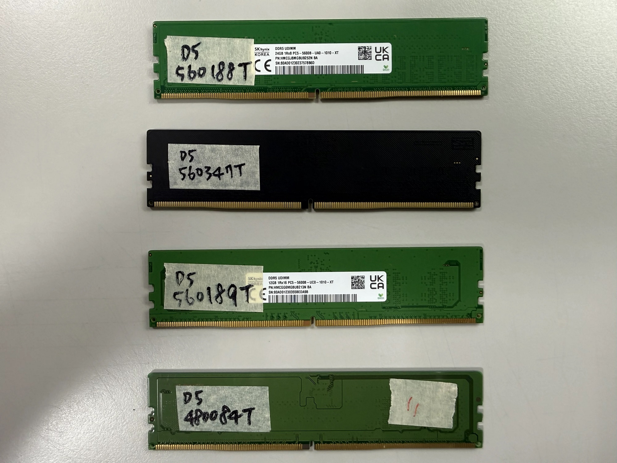 Quatre modules DDR5 U-DIMM SK hynix avec étiquettes (ex. 560188T, 480084T) posés sur une surface blanche.