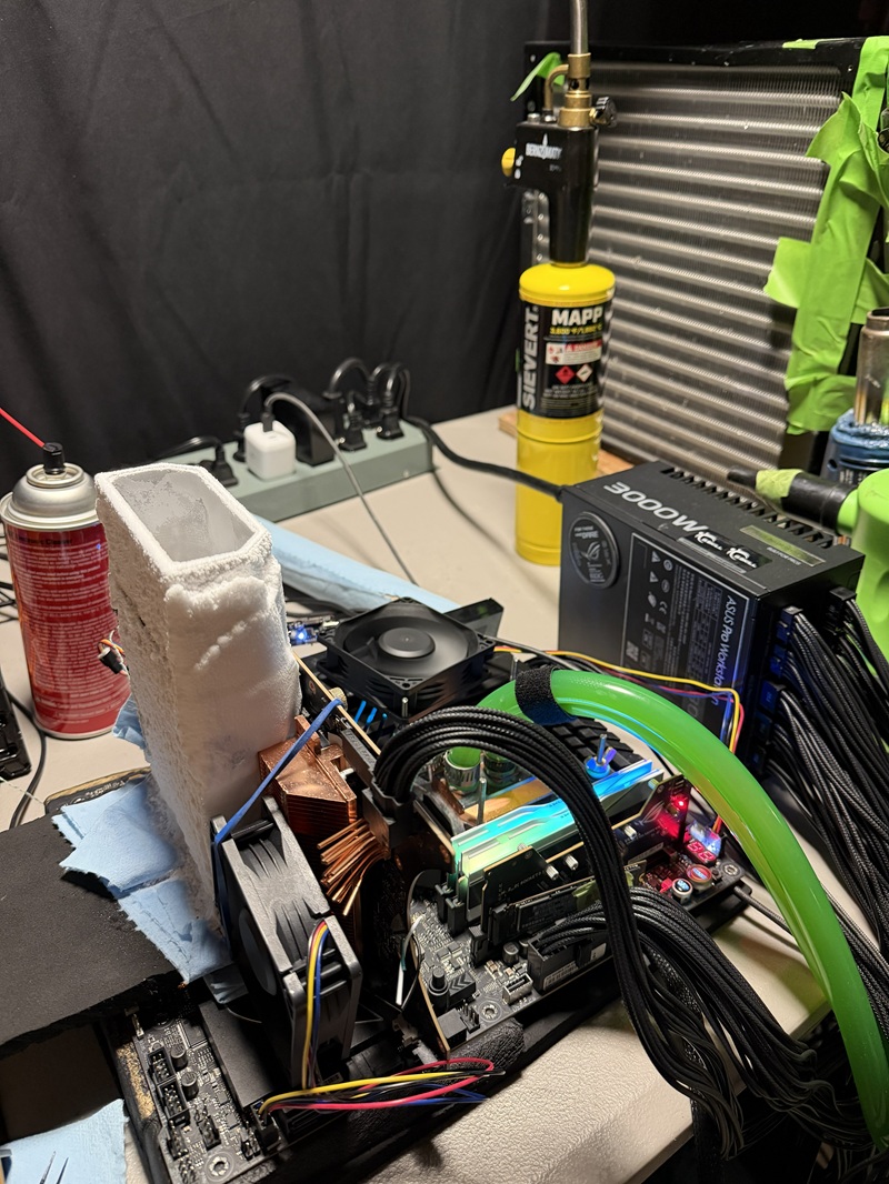 A computer setup with liquid nitrogen cooling is overclocked, featuring a '3000W' power supply and a cooling system using a Sievert MAPP gas torch.