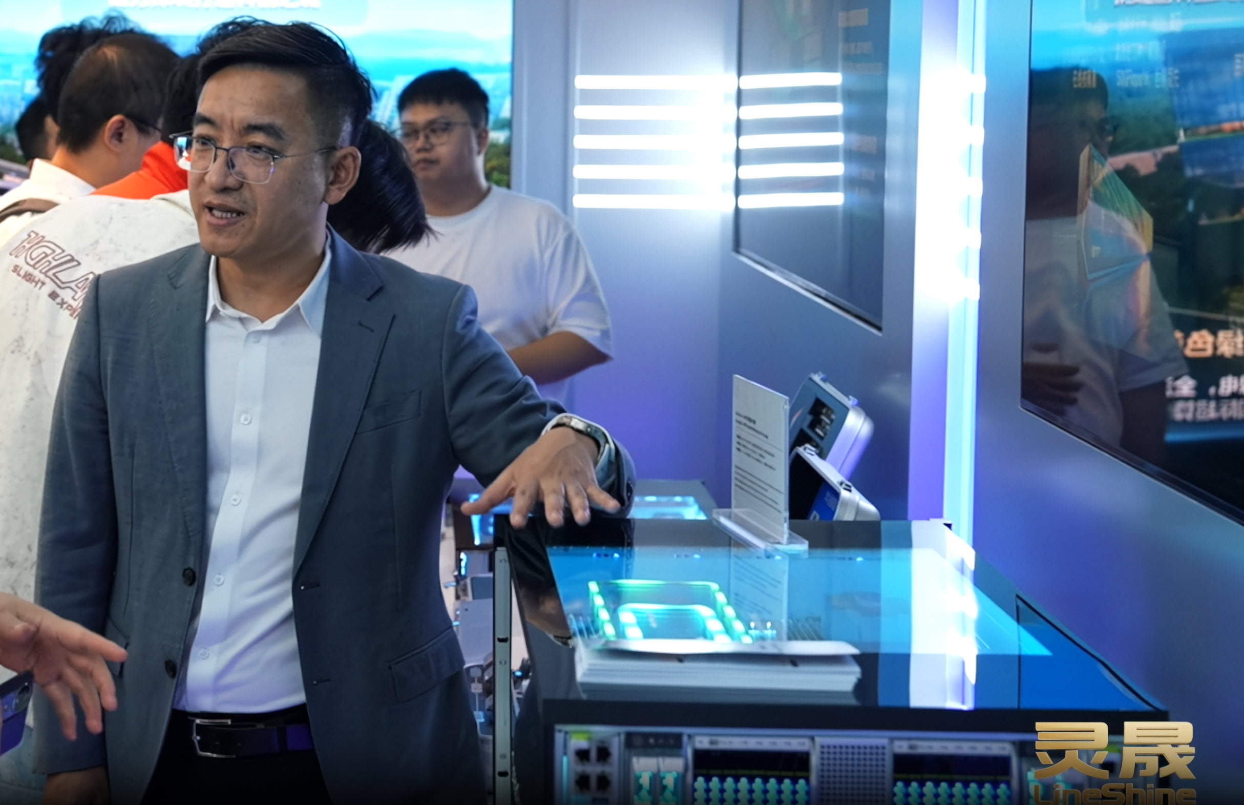 A person in a suit is standing next to a display featuring a LineShine server rack with illuminated hardware components.