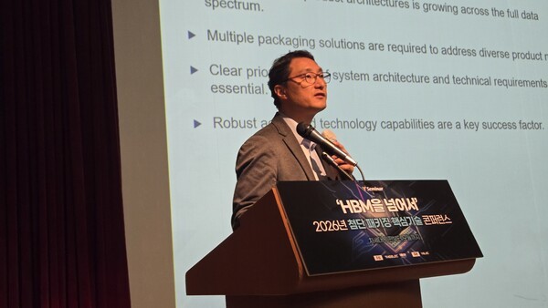 A man is speaking at a podium with a sign reading 'HBM을 넘어서' at a conference, with a presentation slide in the background discussing packaging solutions and technology capabilities.