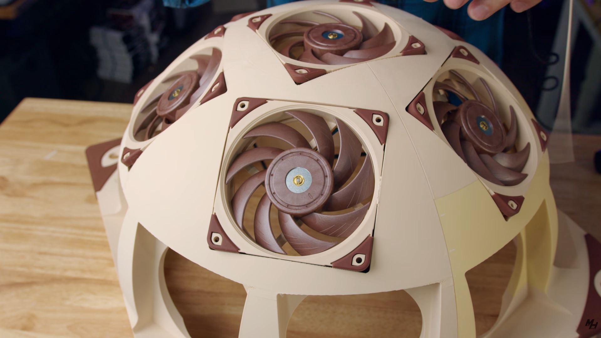 A dome-shaped case featuring five Noctua fans mounted on its surface is being examined on a wooden table.
