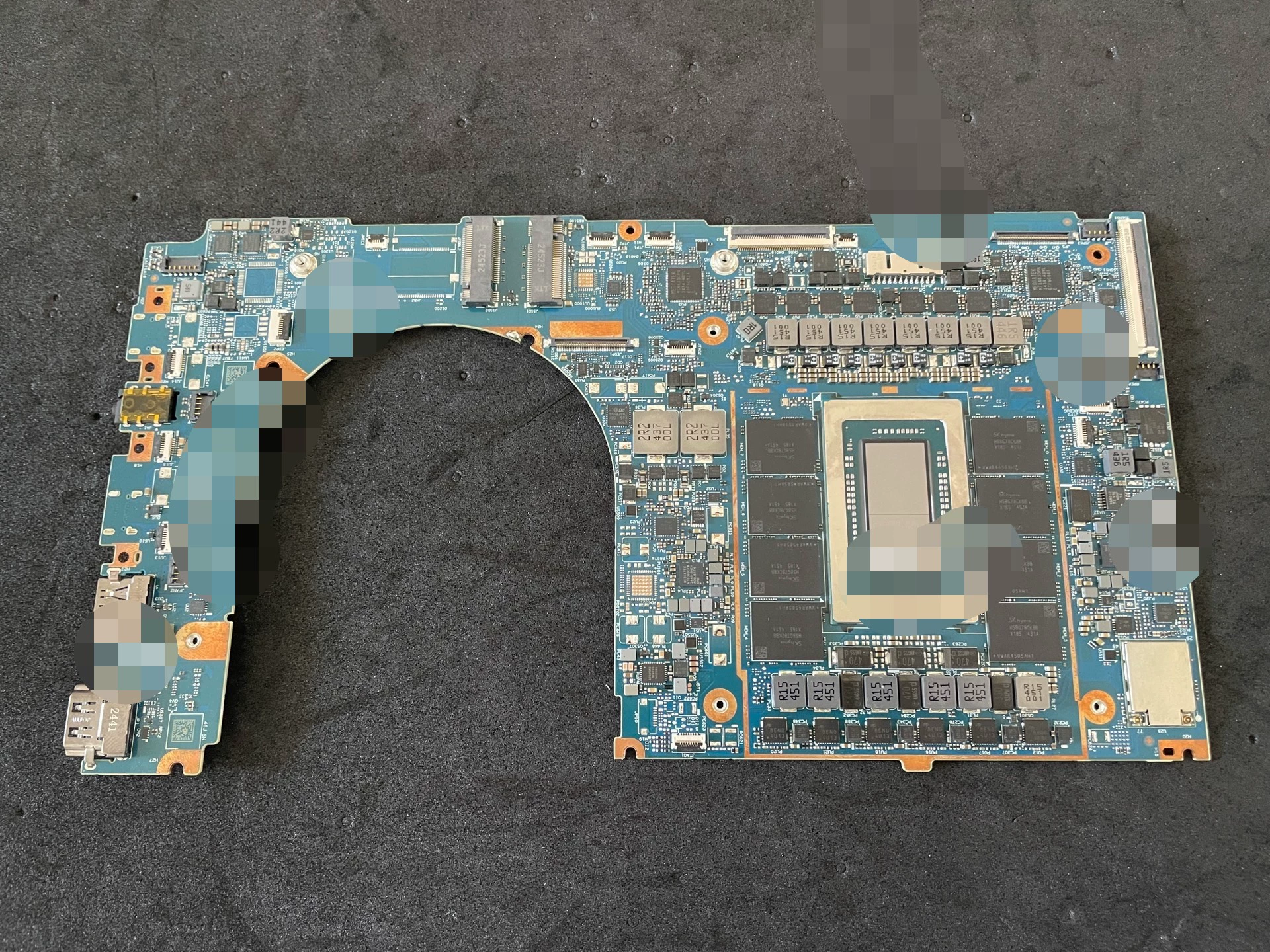 Une carte mère d’ordinateur portable avec une grande puce centrale entourée de condensateurs, ports et connecteurs, posée sur une surface sombre.