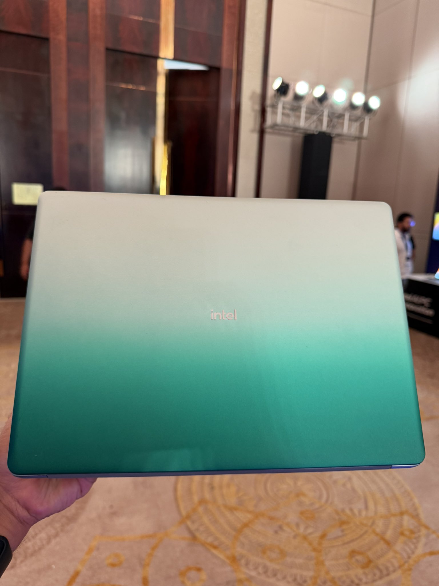 Une personne tient un portable Intel au dégradé vert dans une salle de conférence.