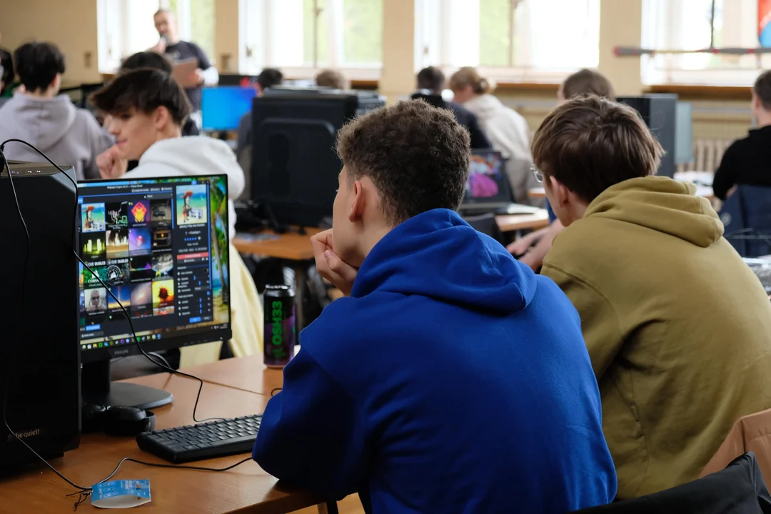 Students sitting in a classroom, with one using a computer displaying a game selection screen.