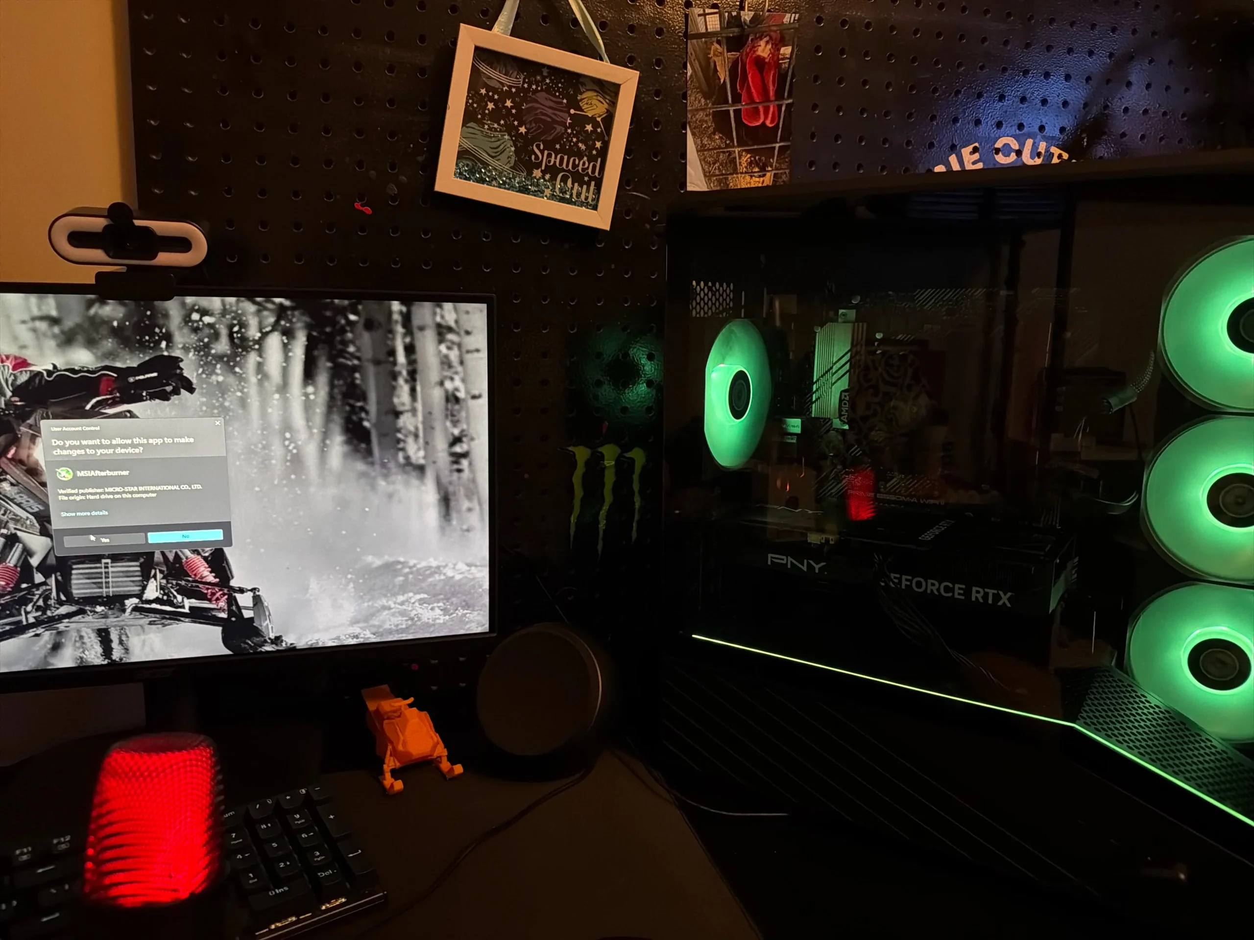 A desktop setup features a PNY GeForce RTX GPU with glowing green fans and a monitor displaying a user account control prompt from 'MSI Afterburner'.