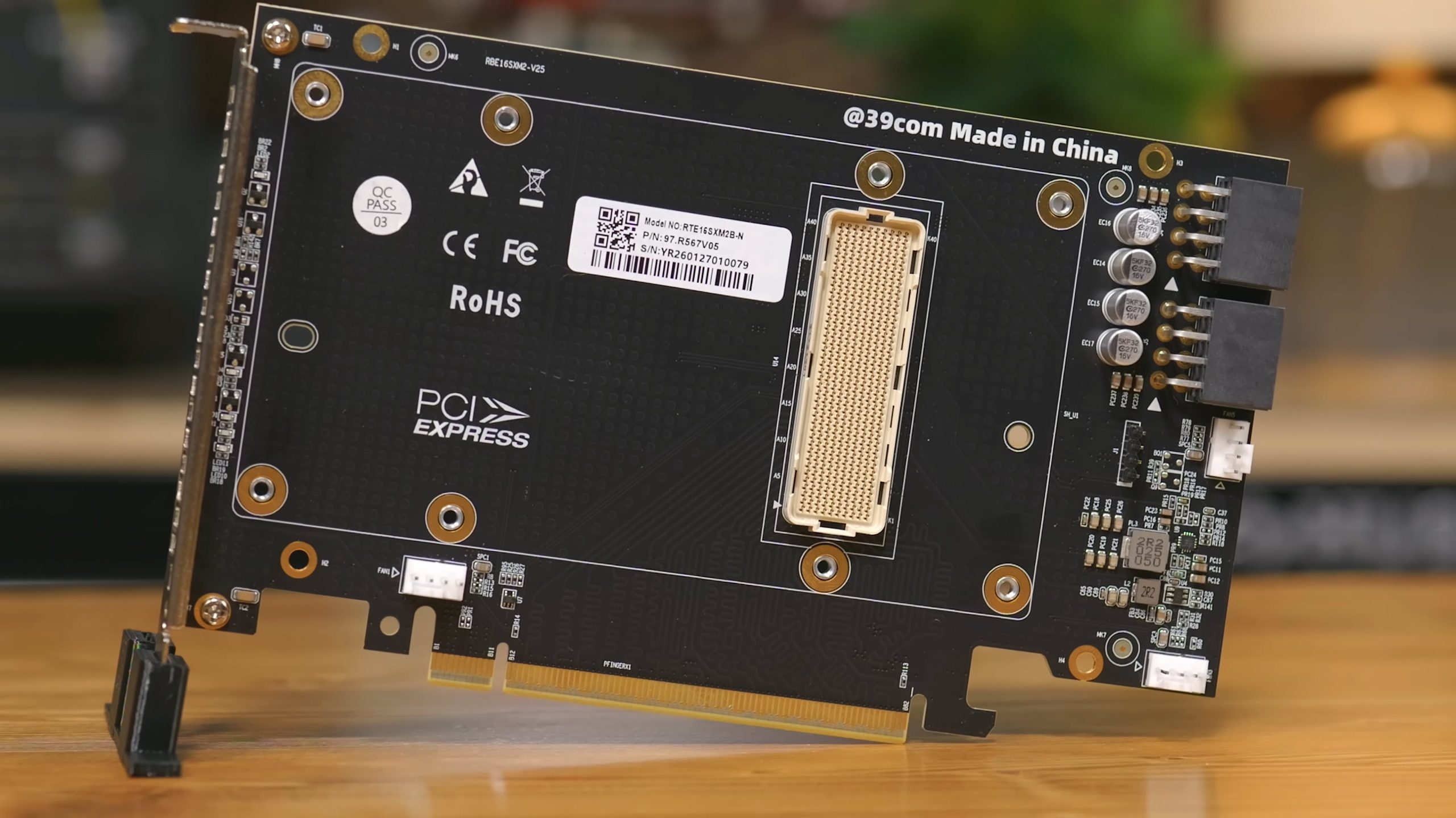 A PCI Express card labeled 'Model No: RTE165KMB2-N' and 'P/N: 9R.5667V6' with various electronic components on a wooden surface.