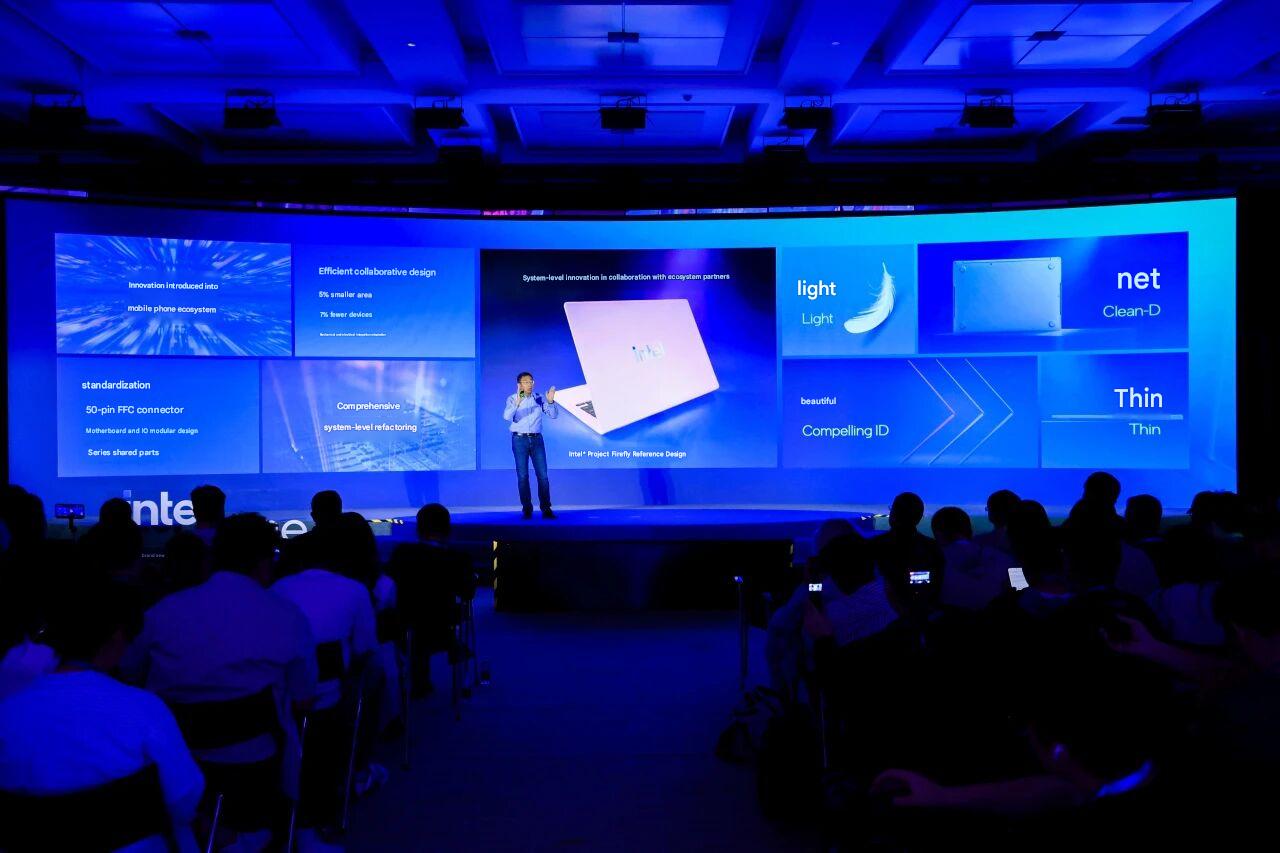 An Intel presenter stands on stage in front of a display featuring the 'Intel Project Firefly Reference Design' laptop and various design elements like 'light' and 'thin' at a technology event.