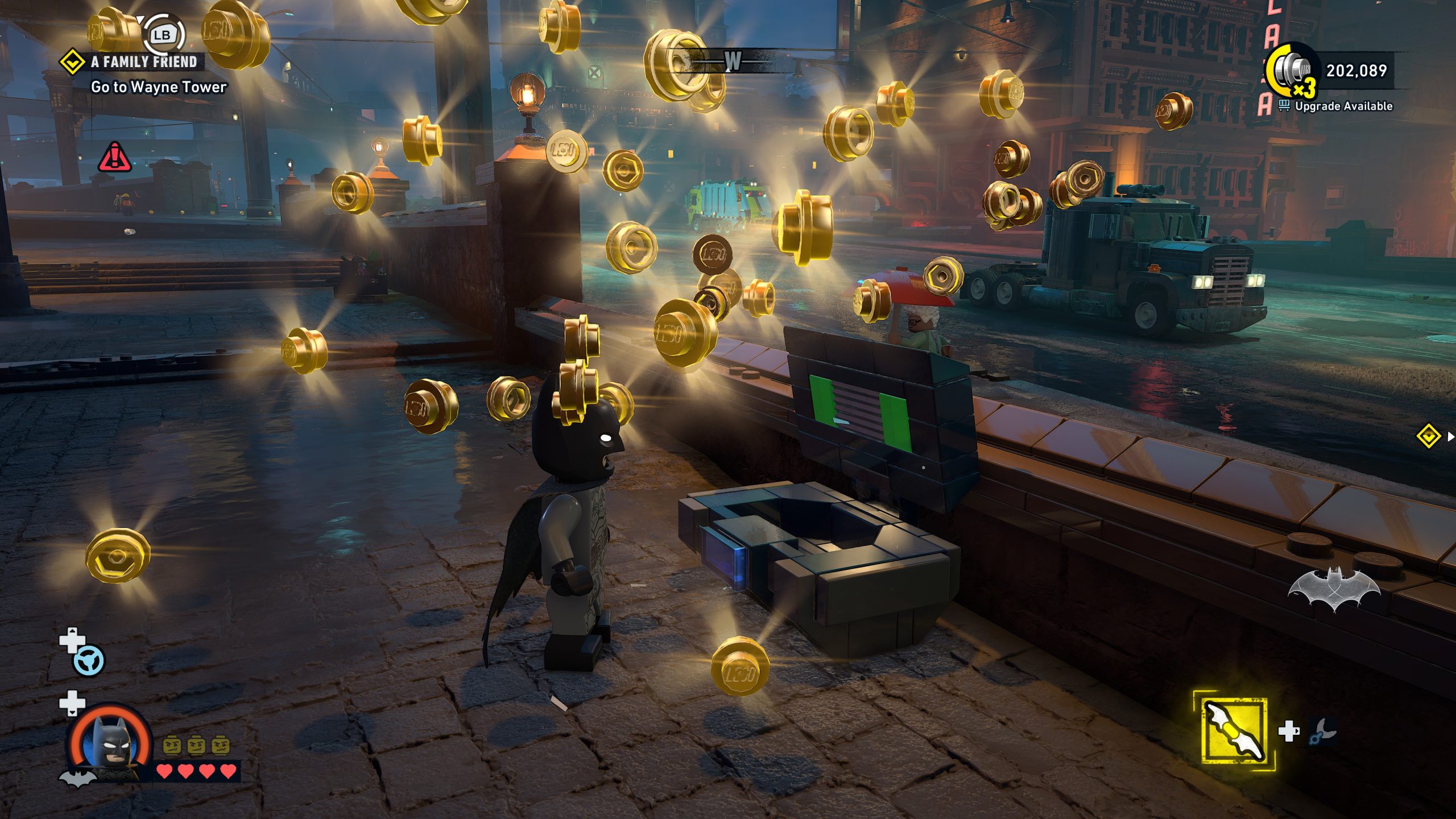 Un personnage de LEGO Batman : Legacy of the Dark Knight collecte des pièces LEGO dorées près d'un écran, avec les objectifs 'Aller à Wayne Tower' affichés en haut à gauche.