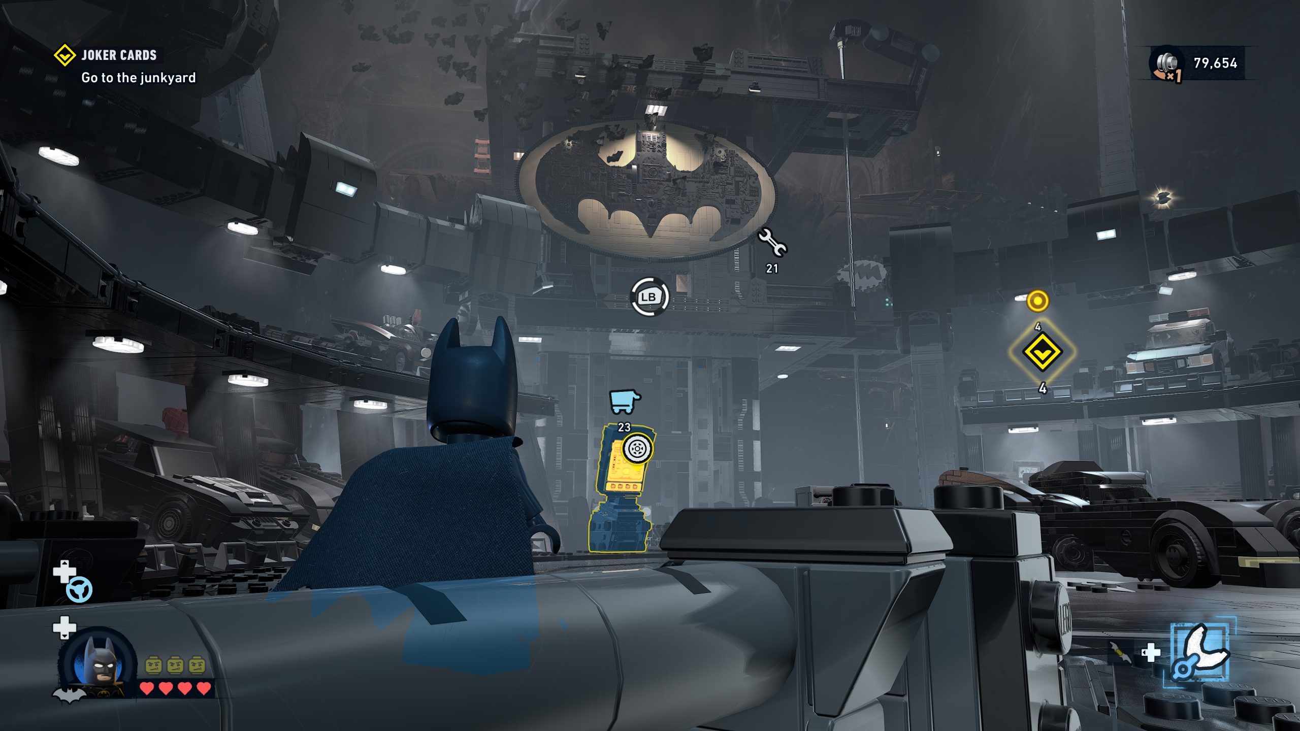 Dans 'LEGO Batman: Legacy of the Dark Knight', Batman dans la Batcave avec véhicules, objectif 'Go to the junkyard.'