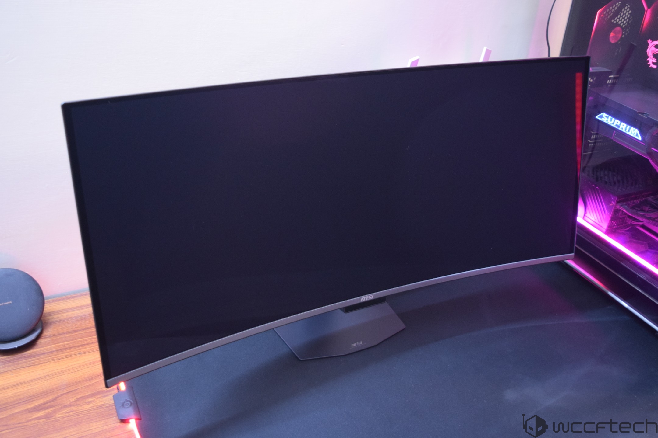 Une femme se tient près d'un écran Samsung 4K 360Hz QD-OLED affichant un jeu de course avec 'Leaderboard' et 'Rapid Racer' visible sur l'écran.