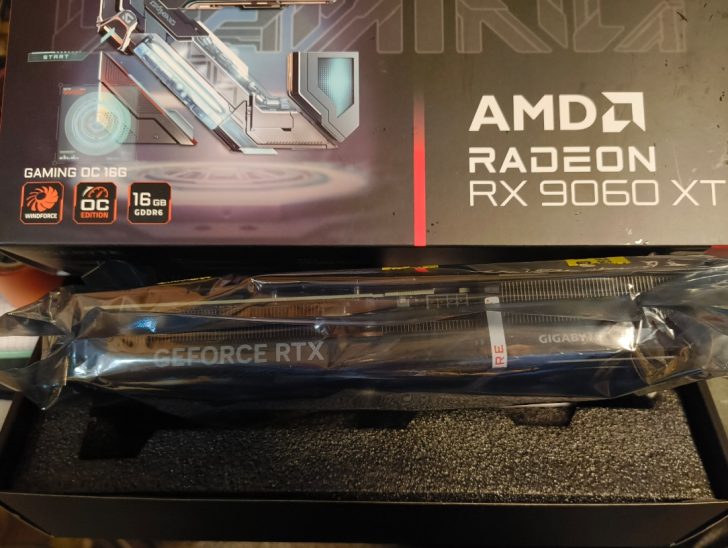 A box for an AMD Radeon RX 9060 XT with 'Gaming OC 16G' and '16 GB GDDR6,' placed above an unopened NVIDIA GeForce RTX card from Gigabyte in packaging.