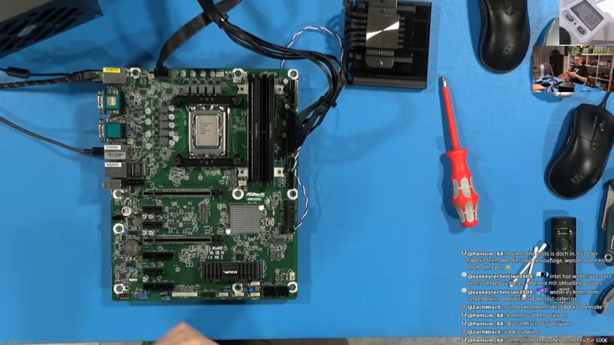 Carte mère ASRock équipée d'un CPU Intel sur une table bleue, avec tournevis, souris noire et ventirad.