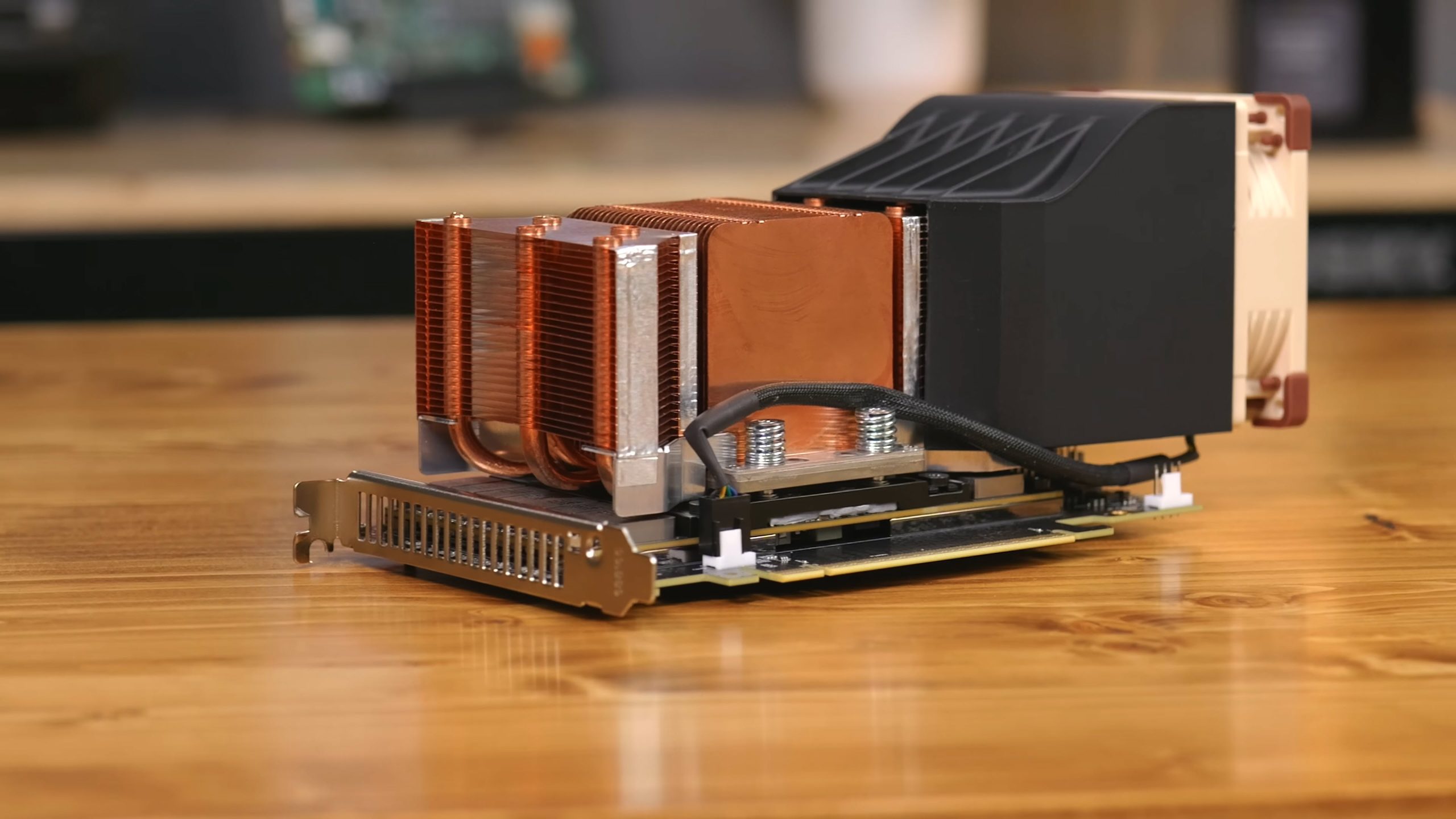 A custom-built cooling solution for a graphics card featuring copper heat sinks and a large fan on a wooden surface.