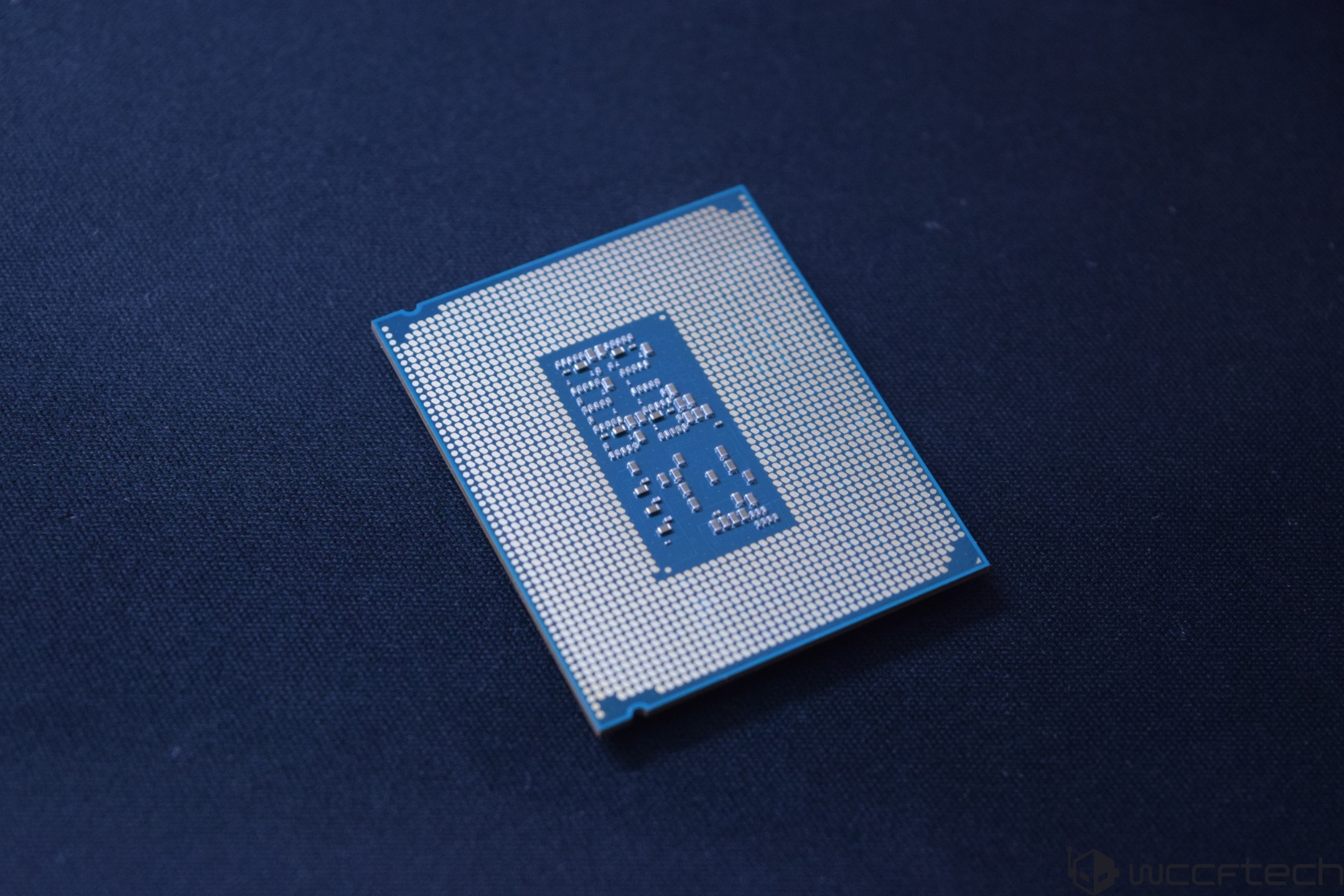 Vue rapprochée du côté contacts d'un CPU Intel avec ses pins et son substrat bleu sur une surface bleue foncée.