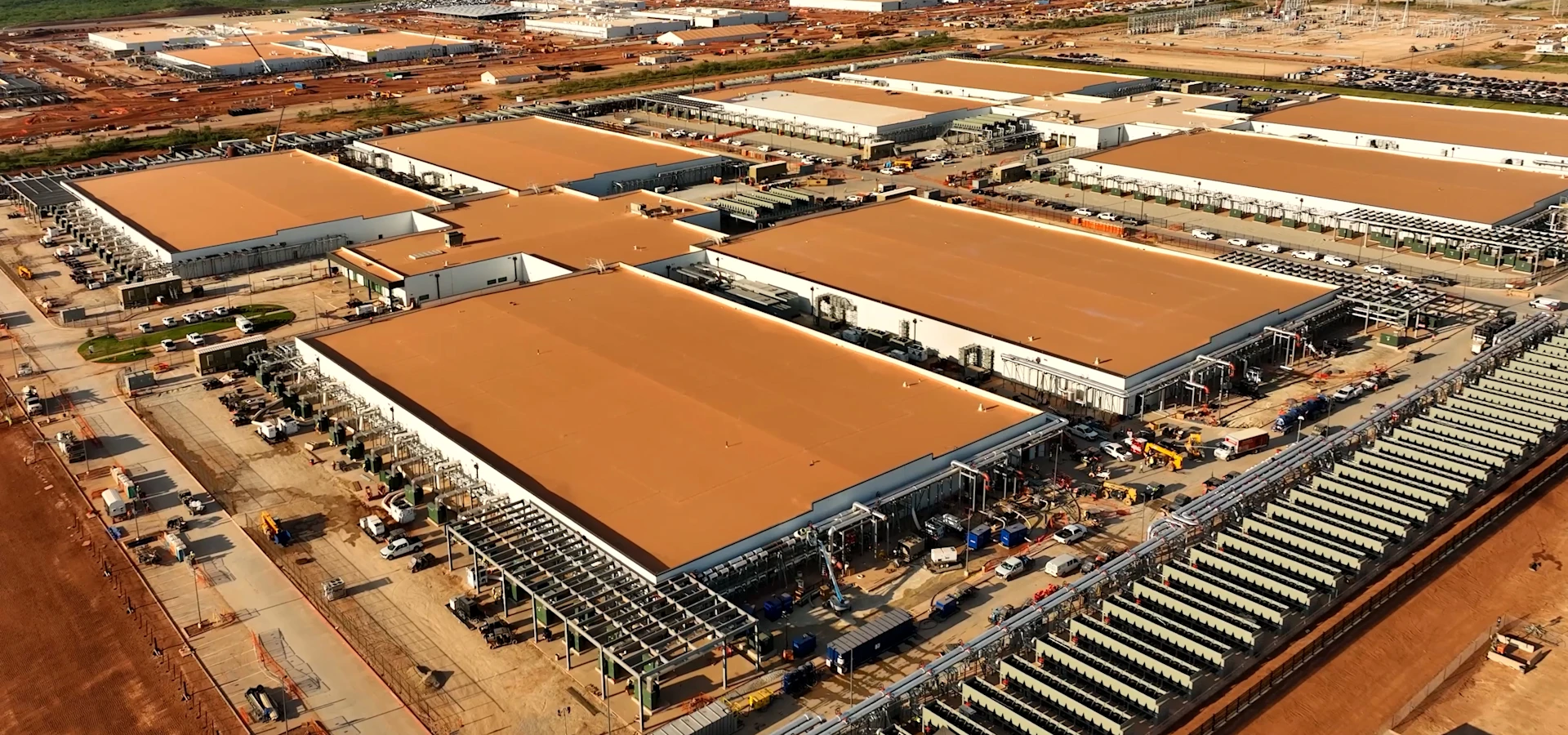 An aerial view of a large industrial complex with several expansive buildings surrounded by construction equipment and vehicles.