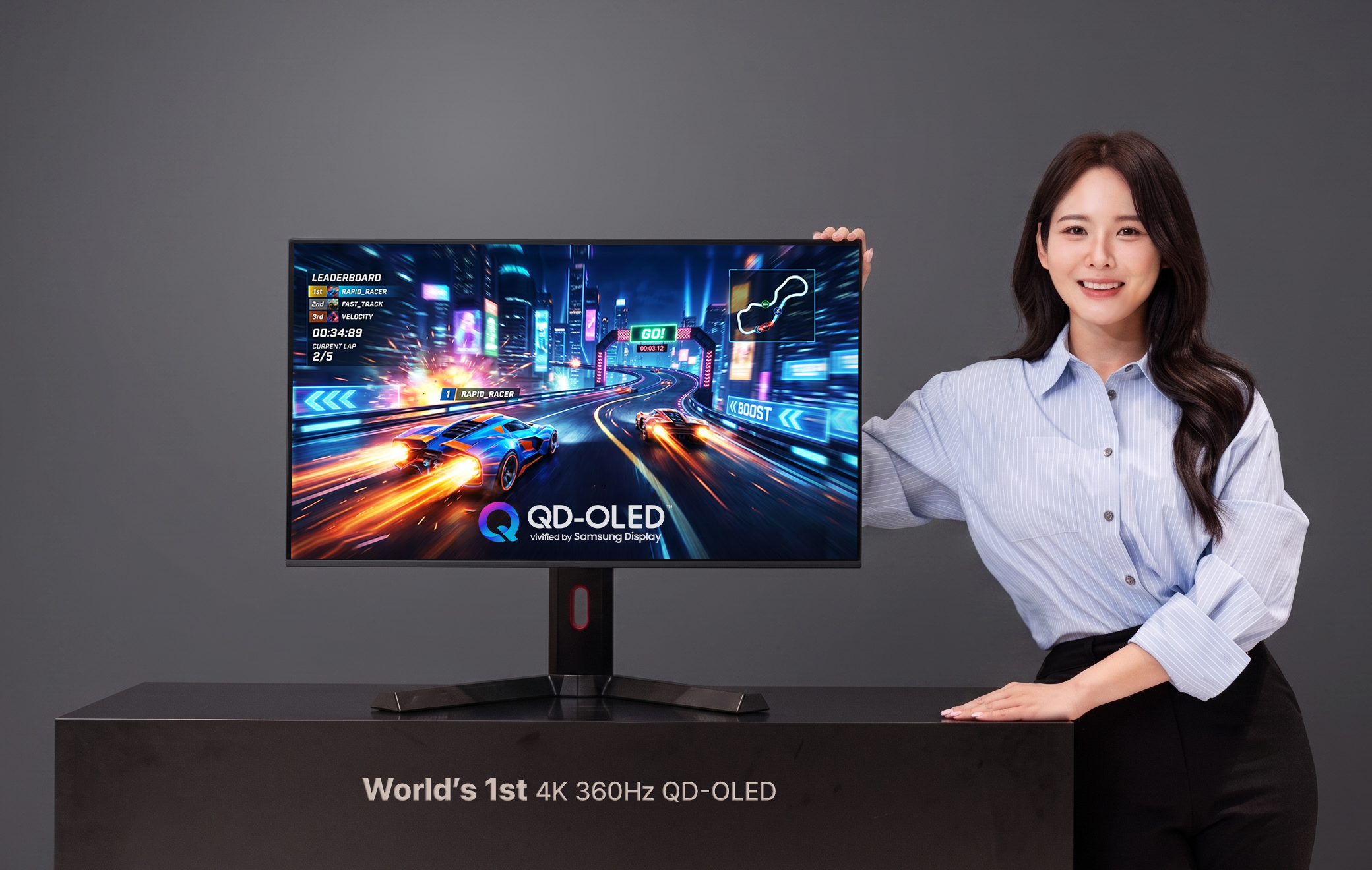 Une femme se tient près d'un écran Samsung 4K 360Hz QD-OLED affichant un jeu de course avec 'Leaderboard' et 'Rapid Racer' visible sur l'écran.