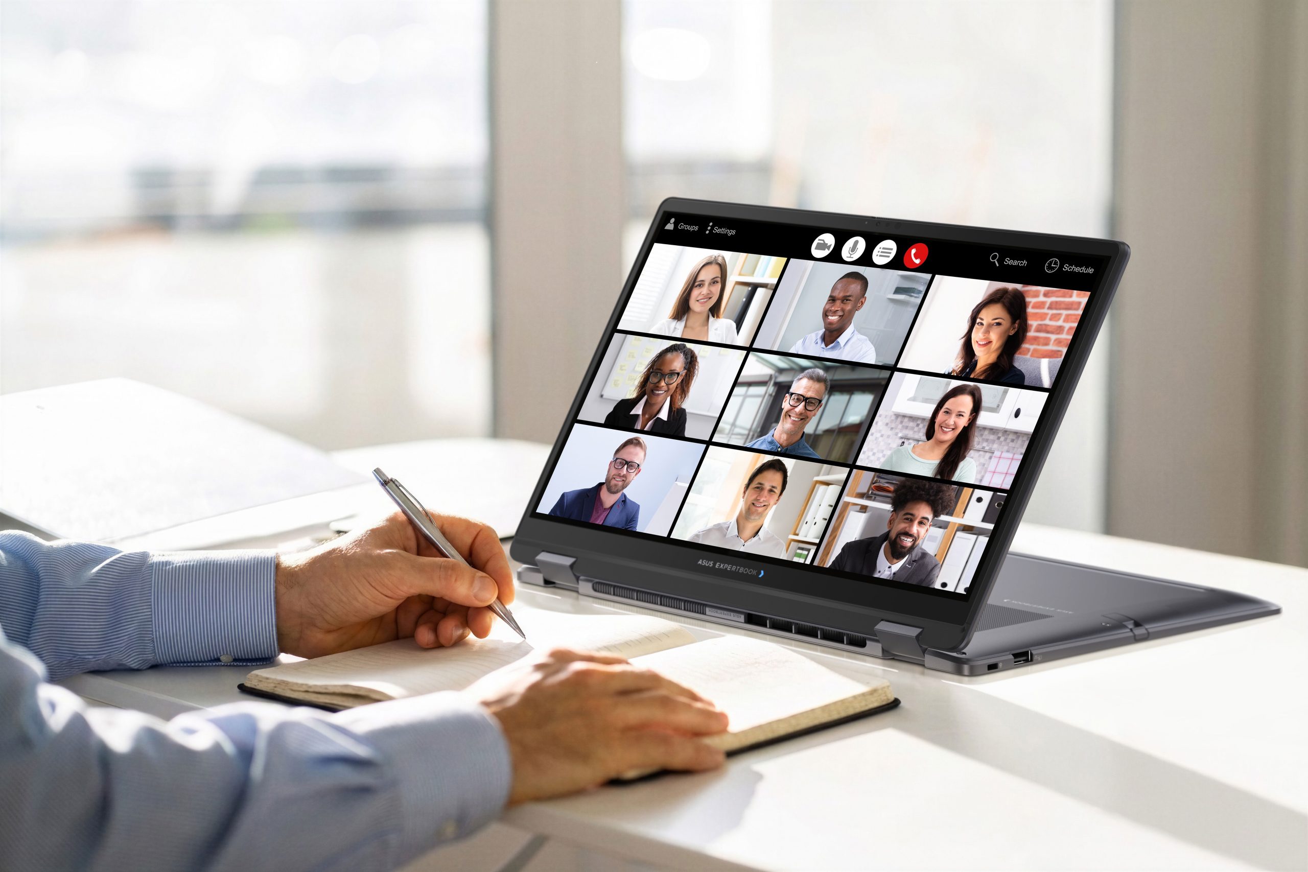 Une personne prend des notes pendant une visioconférence sur un ASUS ExpertBook affichant neuf participants.